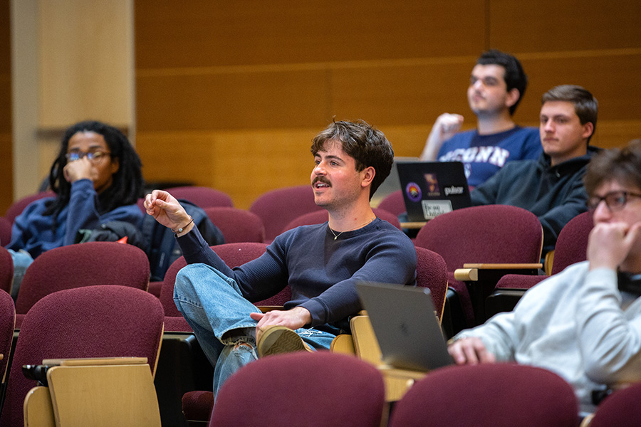 A student in an auditorium asks a question while gesturing.