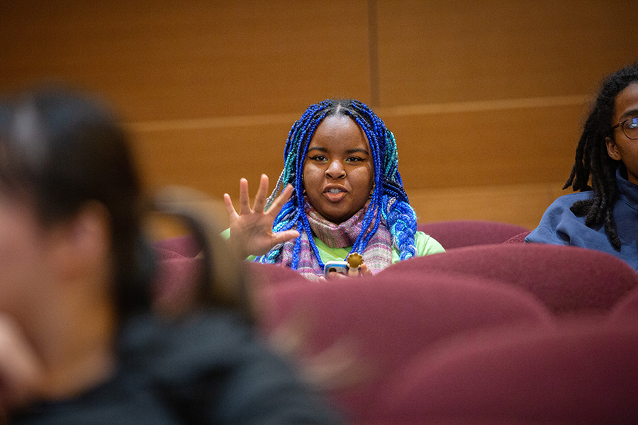 A student with blue hair gestures while asking a question.