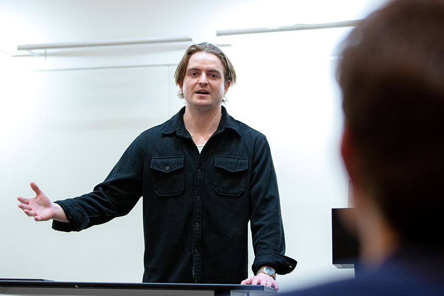 Fritz Bacon gestures while speaking to a lecture hall of full of students.