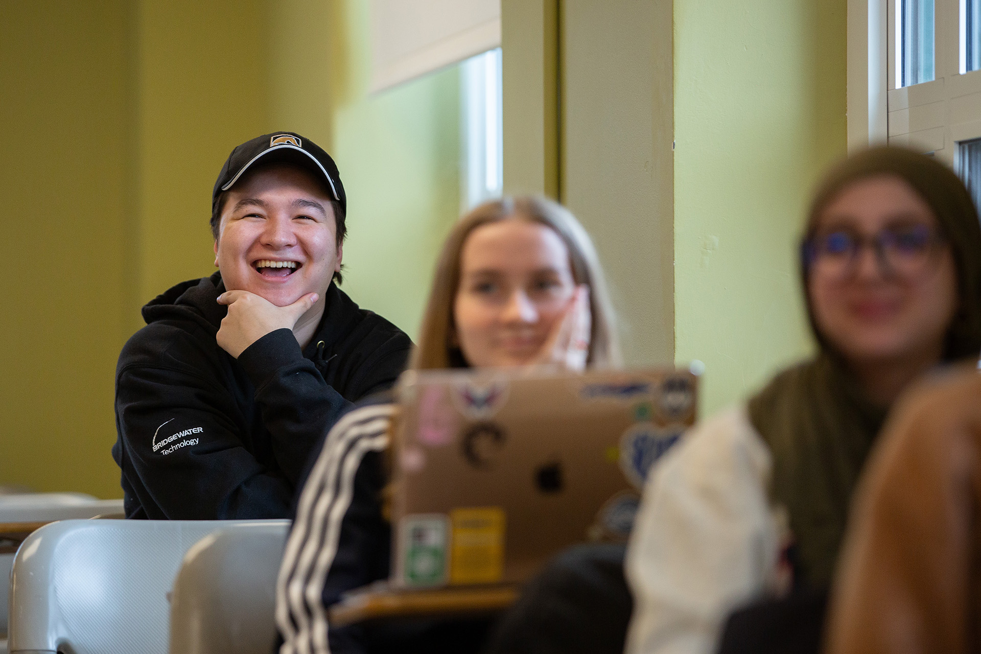 A student wearing a hat laughs during a communication class.